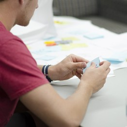 Ein junger Mann sitzt an einem Tisch und erarbeitet Lösungen für eine Aufgabe